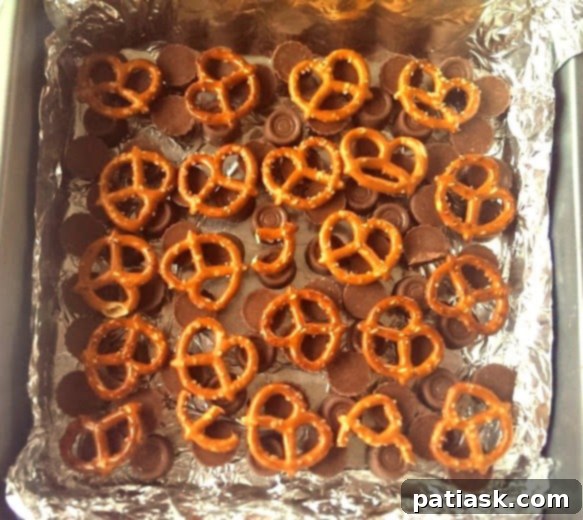 Sweet and Salty Rolo Reese's Pretzel Fudge 4 Rolo Reeses PB Pretzel Fudge being poured into a pan with candy and pretzels.