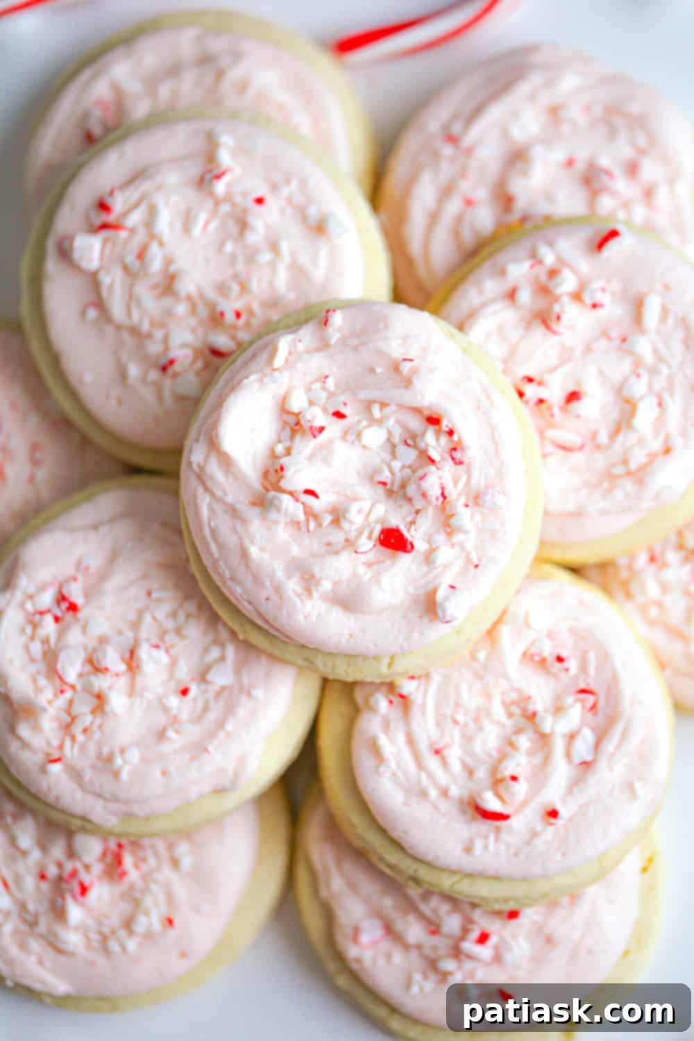 Peppermint Swirl Cookies 3 A close-up shot of candy cane frosted sugar cookies stacked on a white plate with holiday decorations.