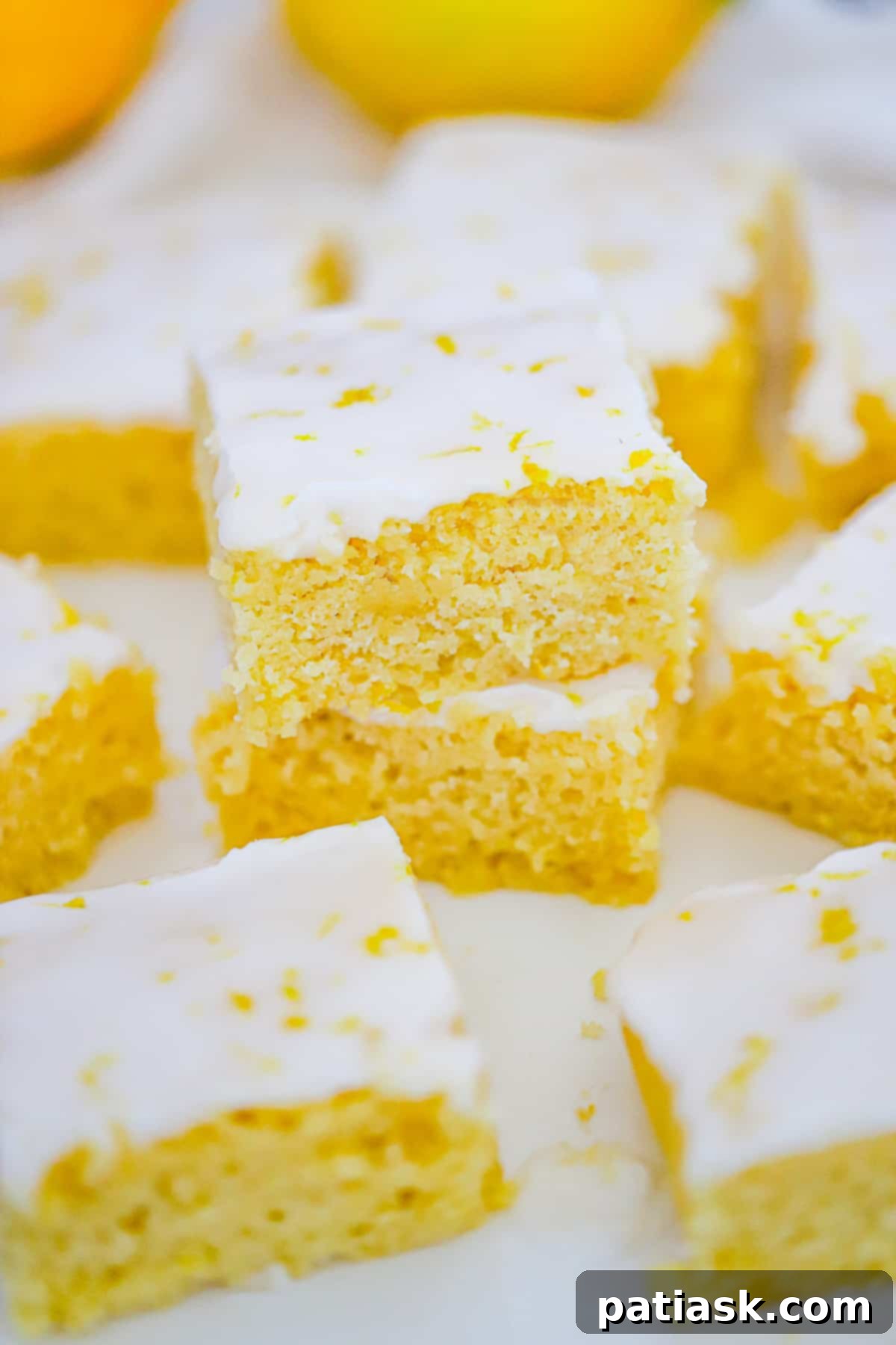 Stack of four homemade lemon brownies, with a few slices of fresh lemon, ready to be enjoyed.