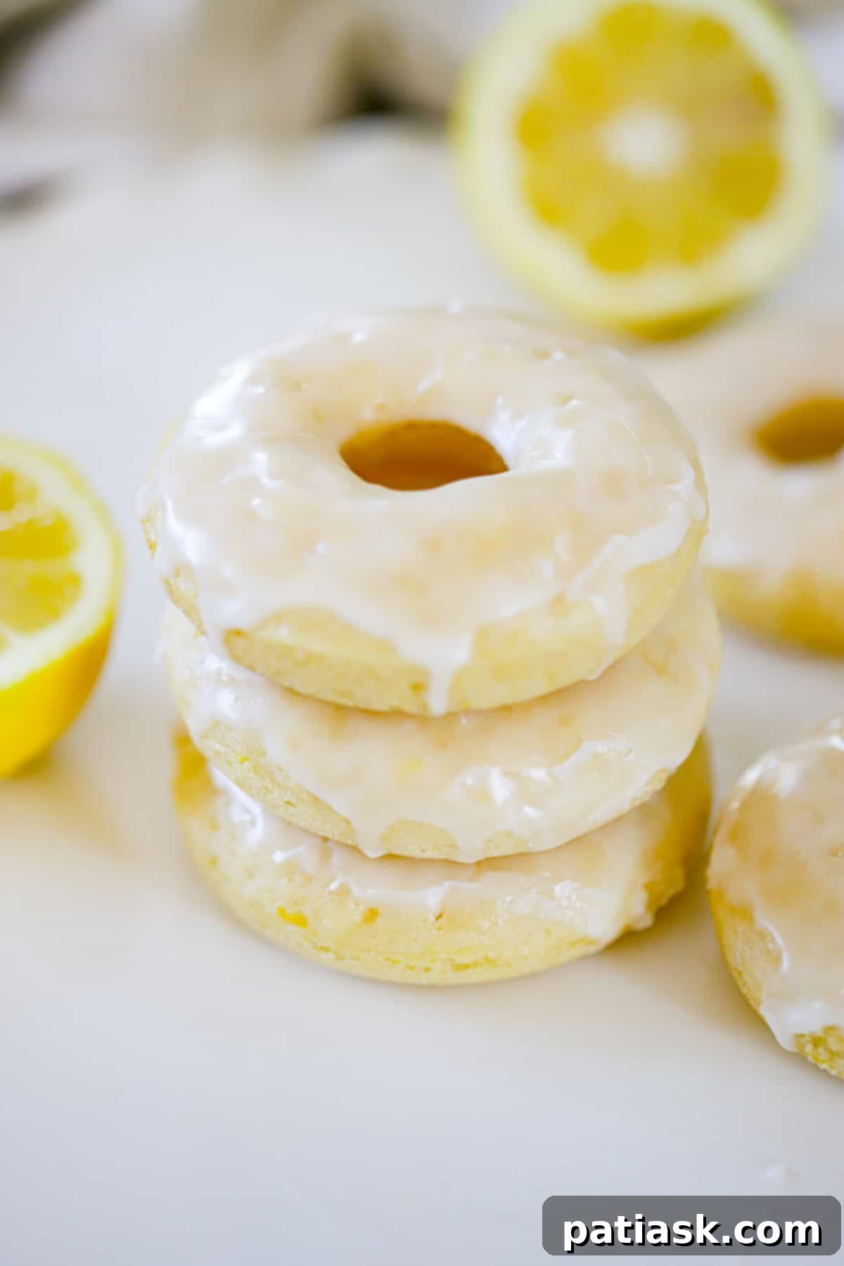 Lemon Zing Donuts 3 A stack of lemon glazed donuts on a cooling rack, glistening with fresh lemon glaze and garnished with zest.