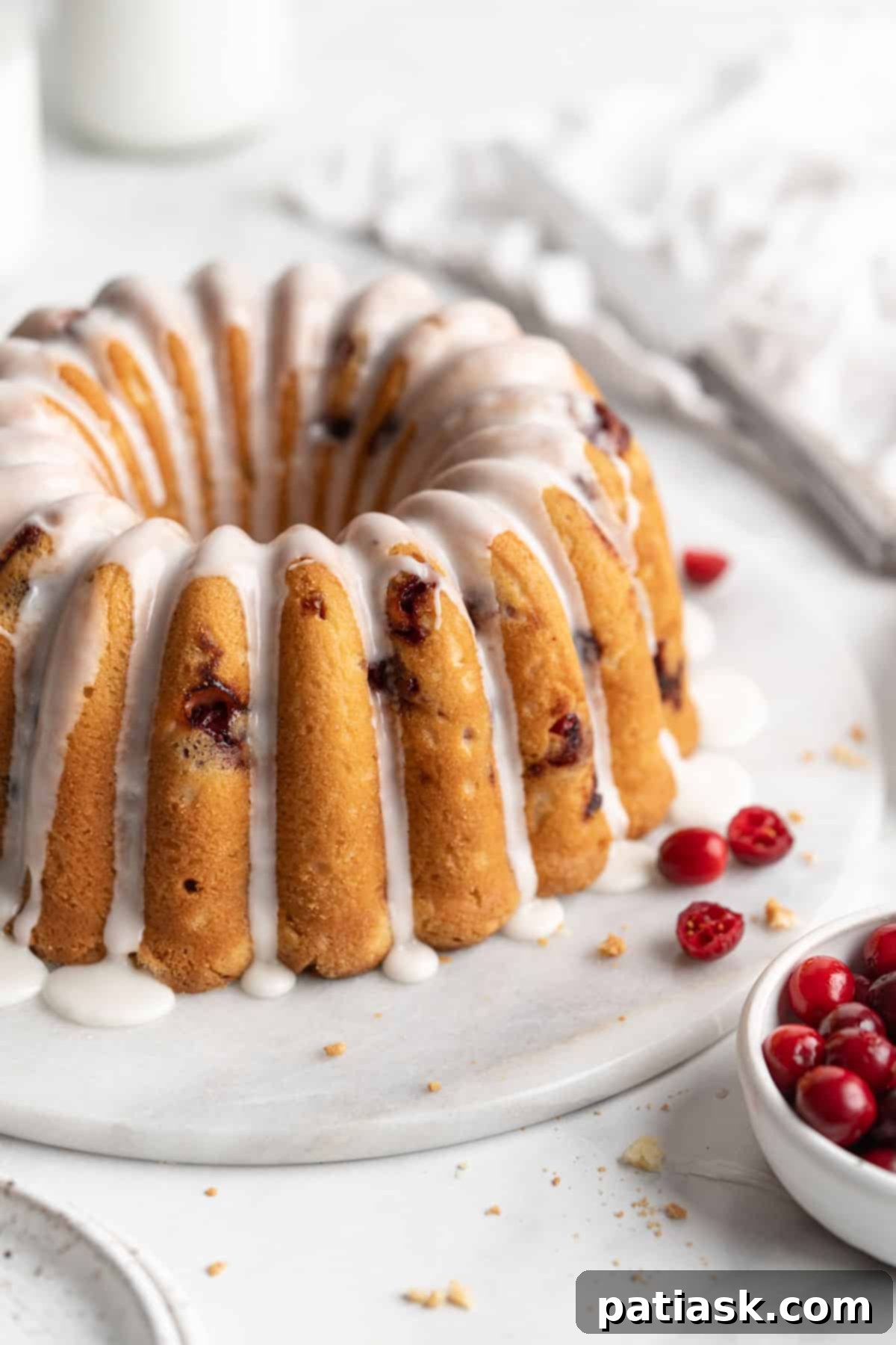 A beautifully glazed cranberry orange bundt cake on a serving plate, ready to be sliced.