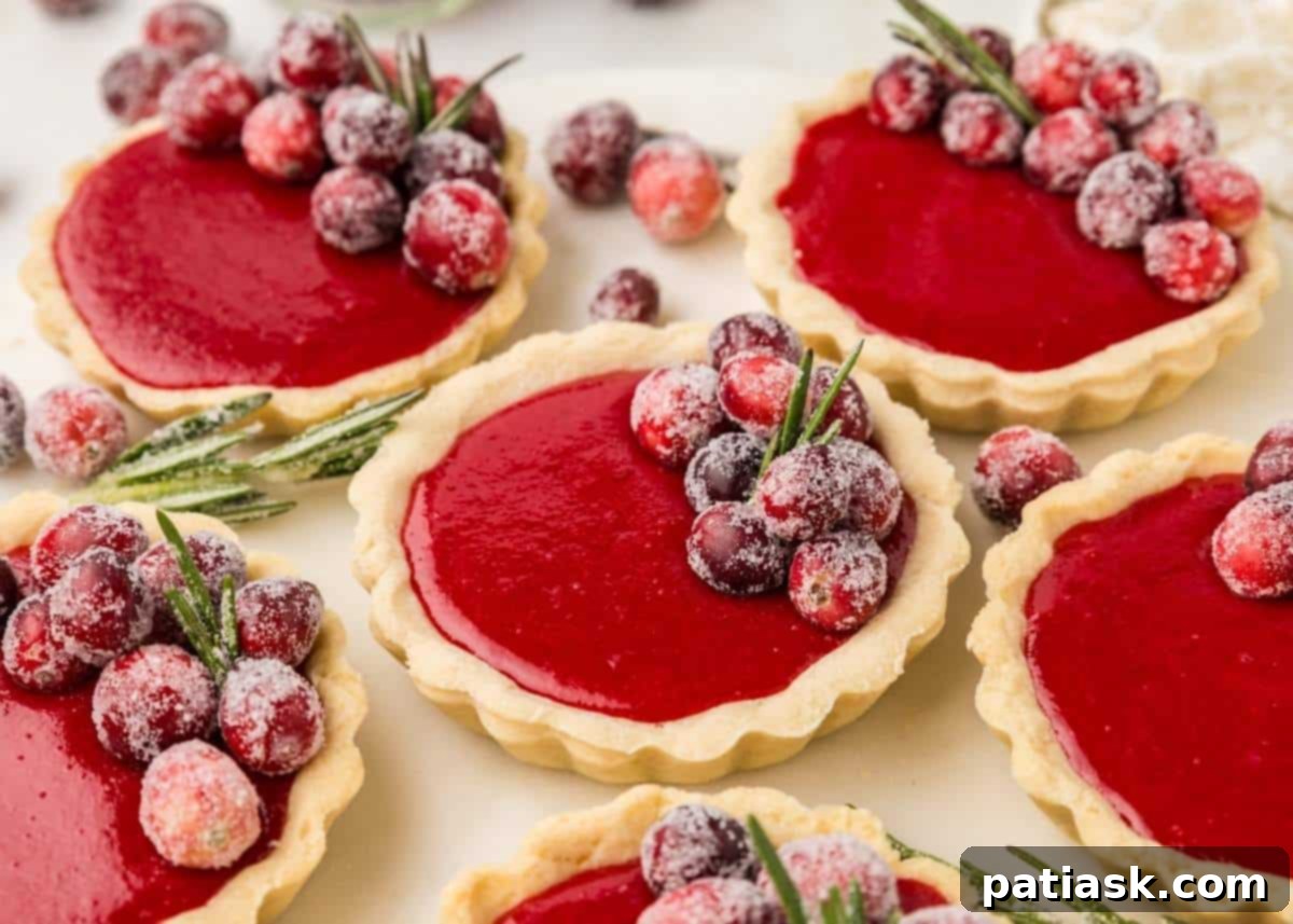 Several mini cranberry tartlets with a glossy red filling, artfully arranged on a platter.