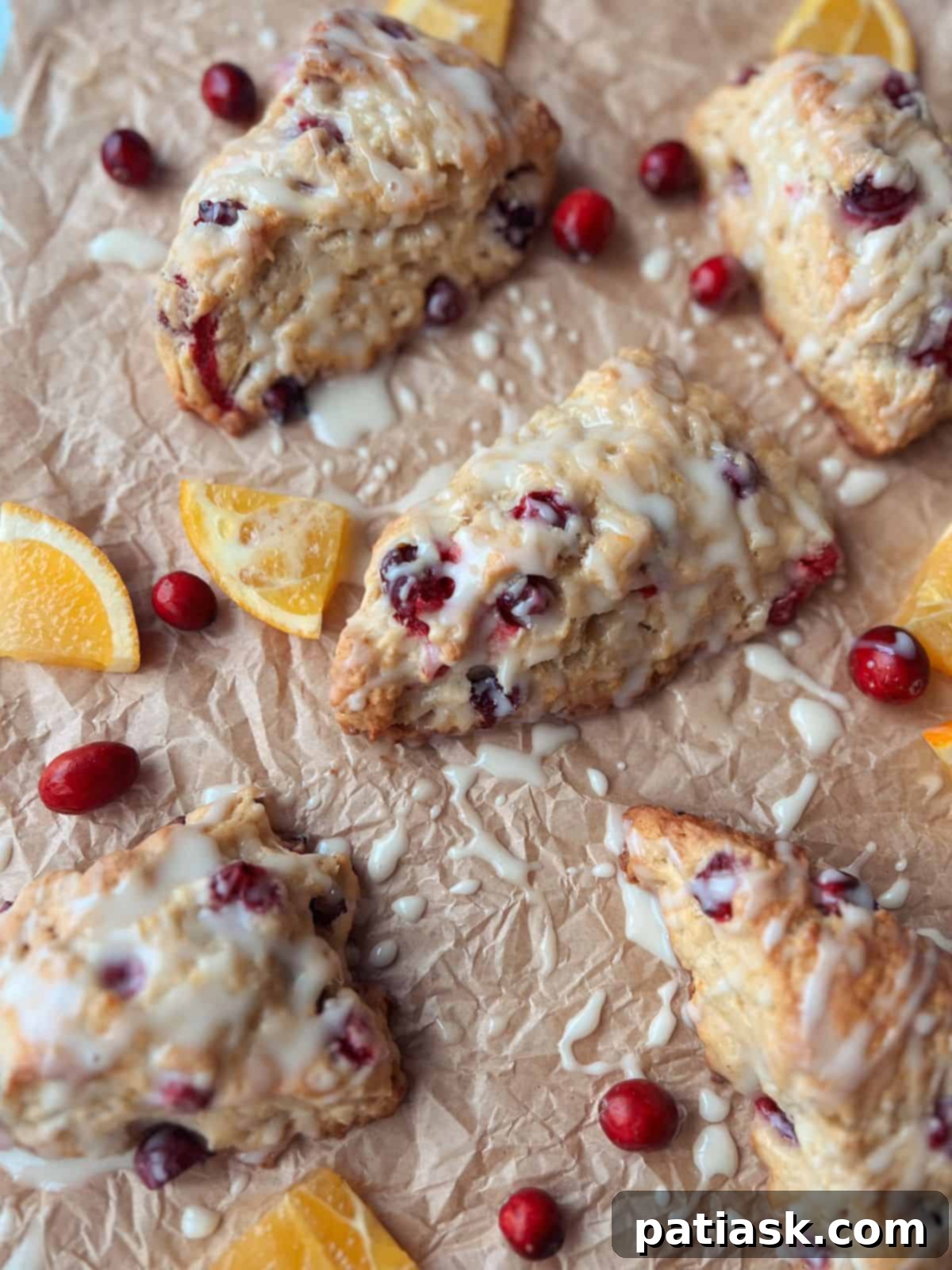 Freshly baked cranberry orange scones with an orange glaze, cooling on parchment paper.