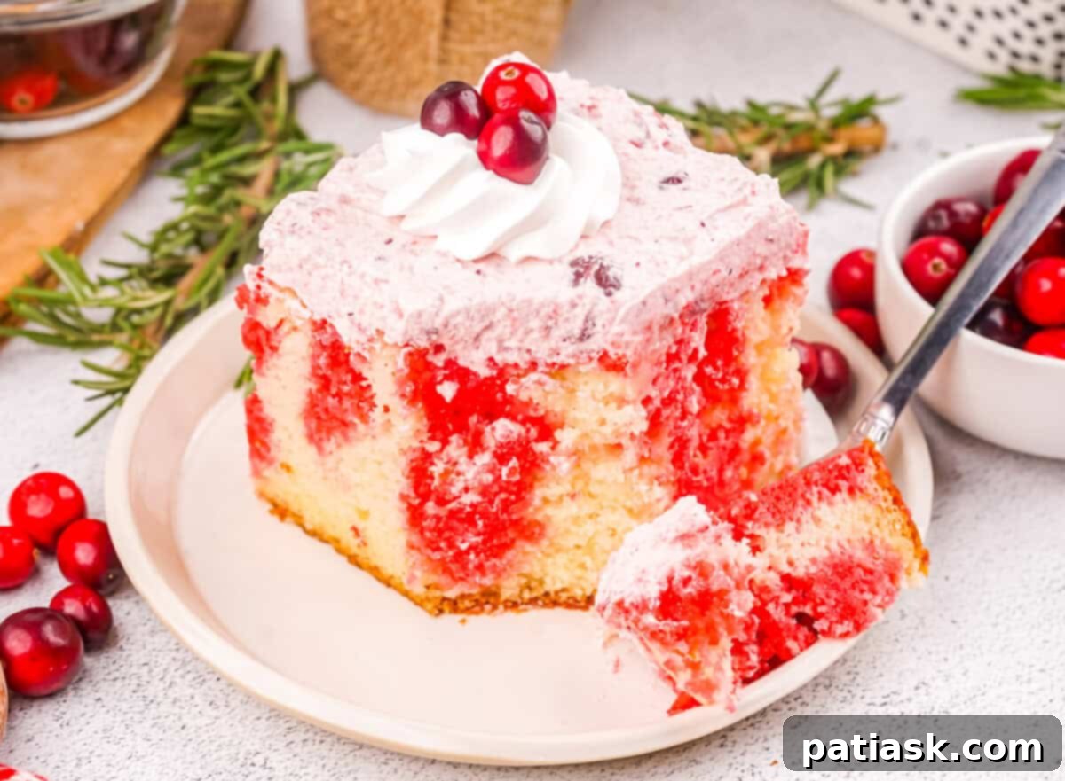 A vibrant cranberry poke cake with a creamy white topping, showing the holes filled with red cranberry jello.