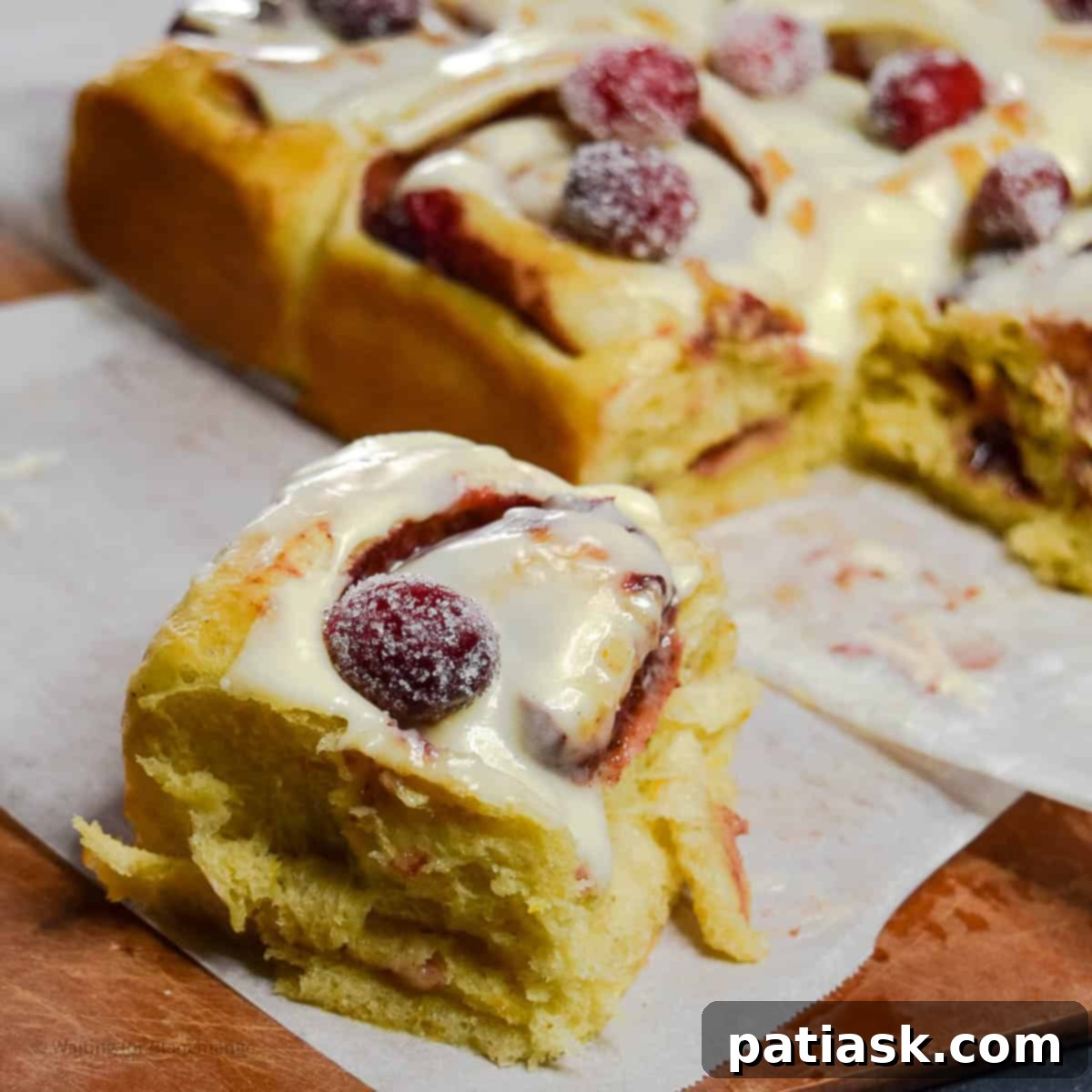 Warm cranberry cinnamon rolls with orange glaze and sugared cranberries, arranged on a baking sheet.