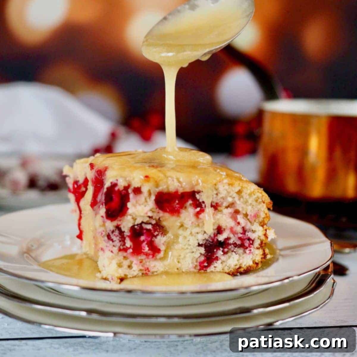 A slice of easy cranberry Christmas cake, drizzled with warm butter sauce, on a festive plate.