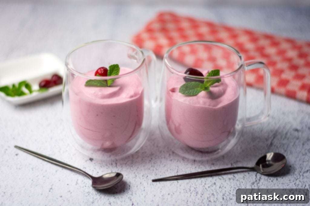 A glass serving dish filled with a light and airy refined sugar-free cranberry mousse, garnished with fresh cranberries.
