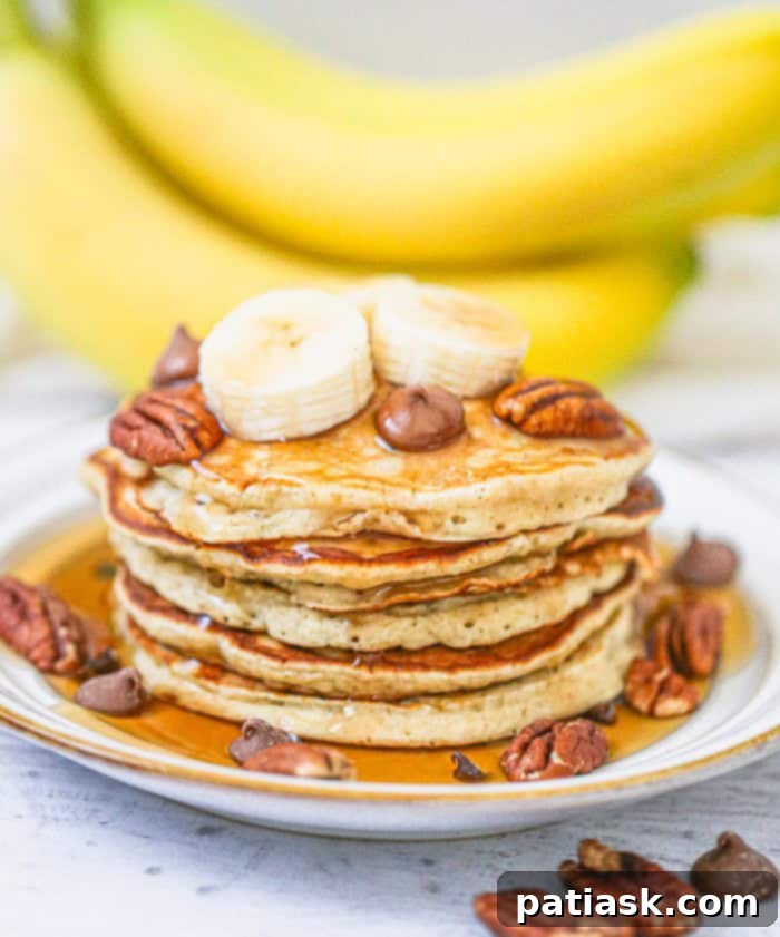 A tall stack of fluffy banana chocolate chip pancakes topped with fresh banana slices, chocolate chips, and syrup, inviting a delightful breakfast or brunch experience.