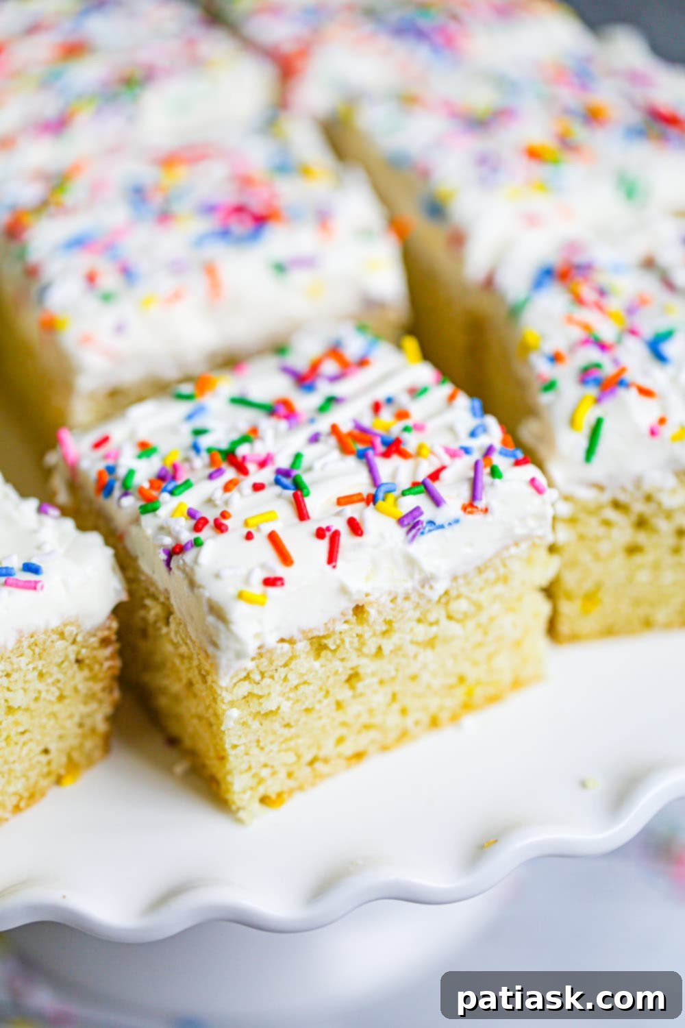 Zesty Lemon Cake 4 A slice of lemon snack cake topped with vanilla frosting and colorful sprinkles on a plate.