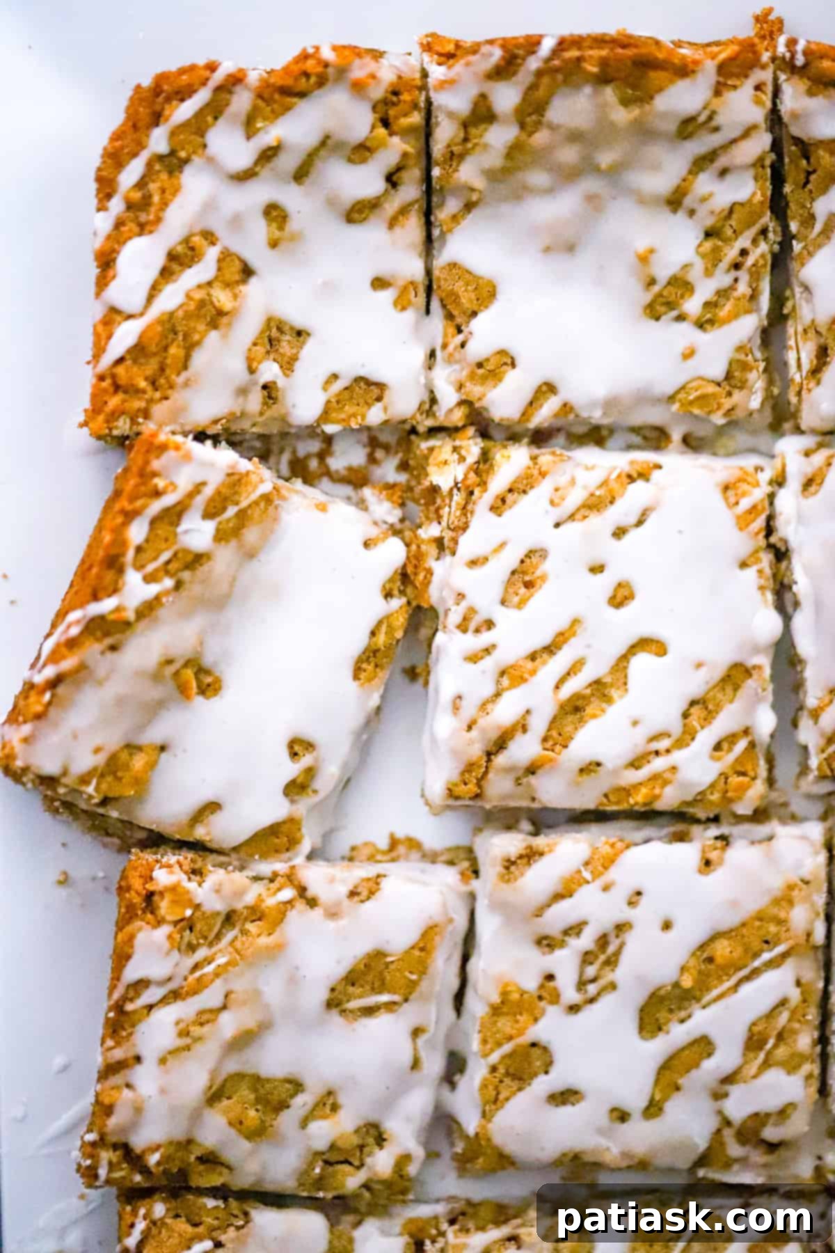 Frosted Oatmeal Bliss Bars 2 Delicious Iced Oatmeal Cookie Bars on a cooling rack, ready to be sliced and served.