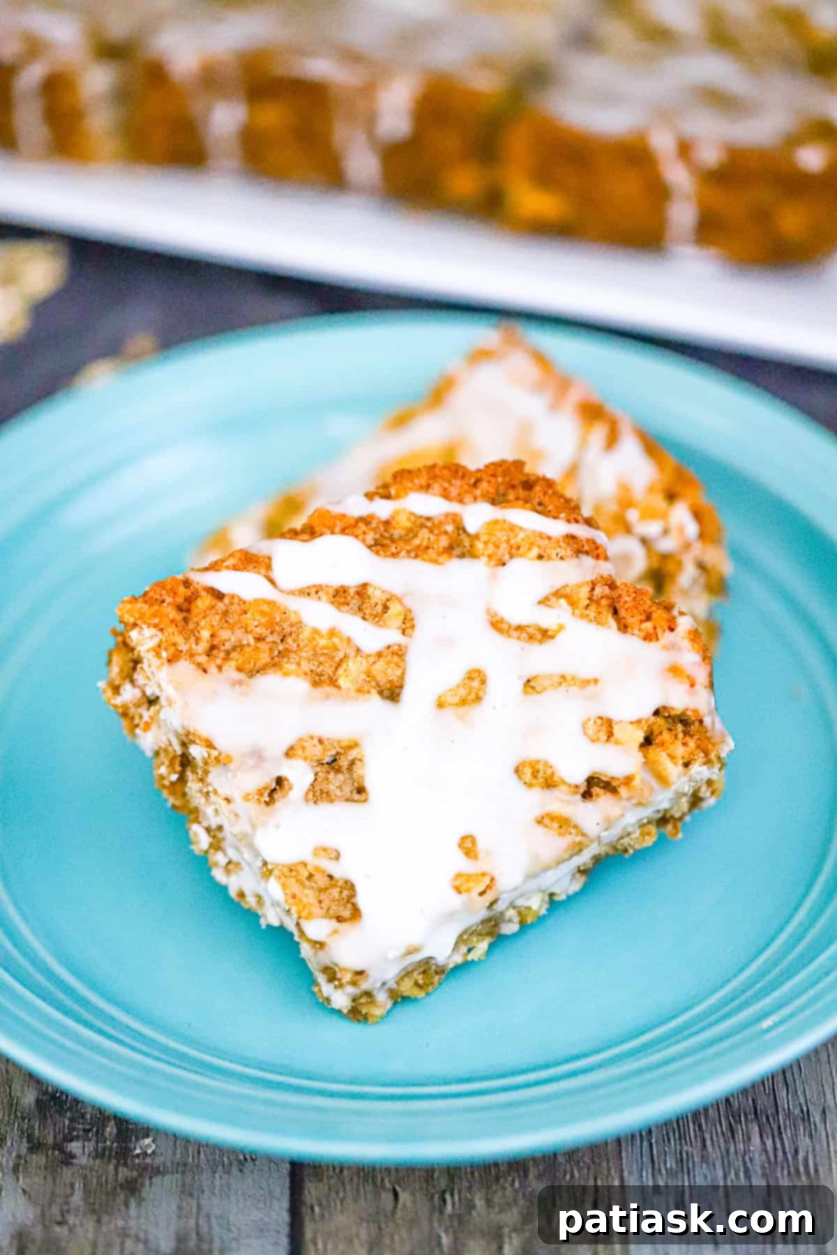 Frosted Oatmeal Bliss Bars 4 Freshly baked old-fashioned iced oatmeal bars, uncut in a baking dish, with a few spoonfuls of vanilla icing ready for spreading.