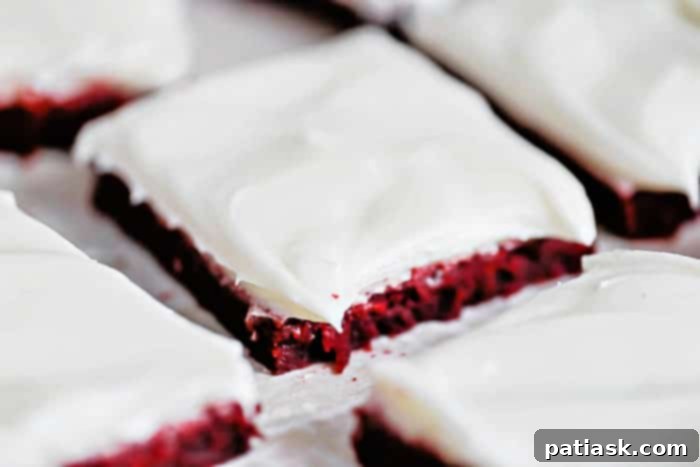 Sliced red velvet cookie bars with cream cheese frosting on a white platter, garnished with sprinkles