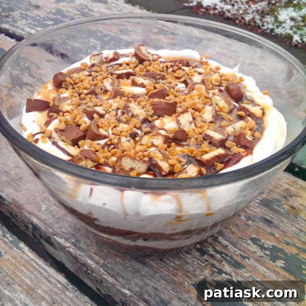 A large serving of Chocolate Caramel Cheesecake Brownie Trifle, garnished with candy and sauces