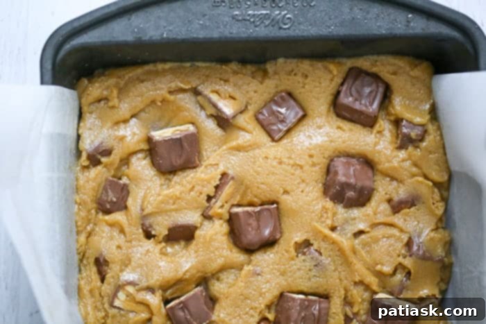 Heavenly Snickers Peanut Butter Blondies 6 Two hands holding a Snickers Peanut Butter Blondie, highlighting its rich texture and delicious appeal.