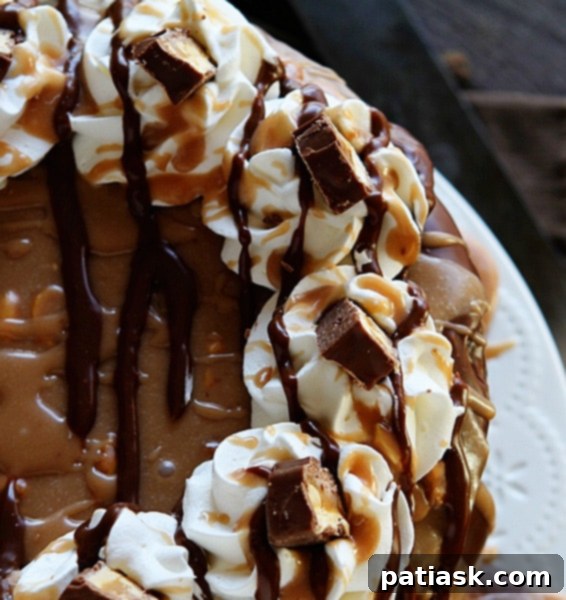 Decadent Snickers Cheesecake Cake with layers of chocolate cake, cheesecake, fudge, caramel, and Snickers.